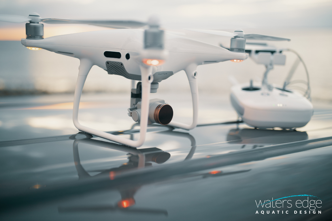 A white drone sits next to its controller on top of a shiny silver surface.